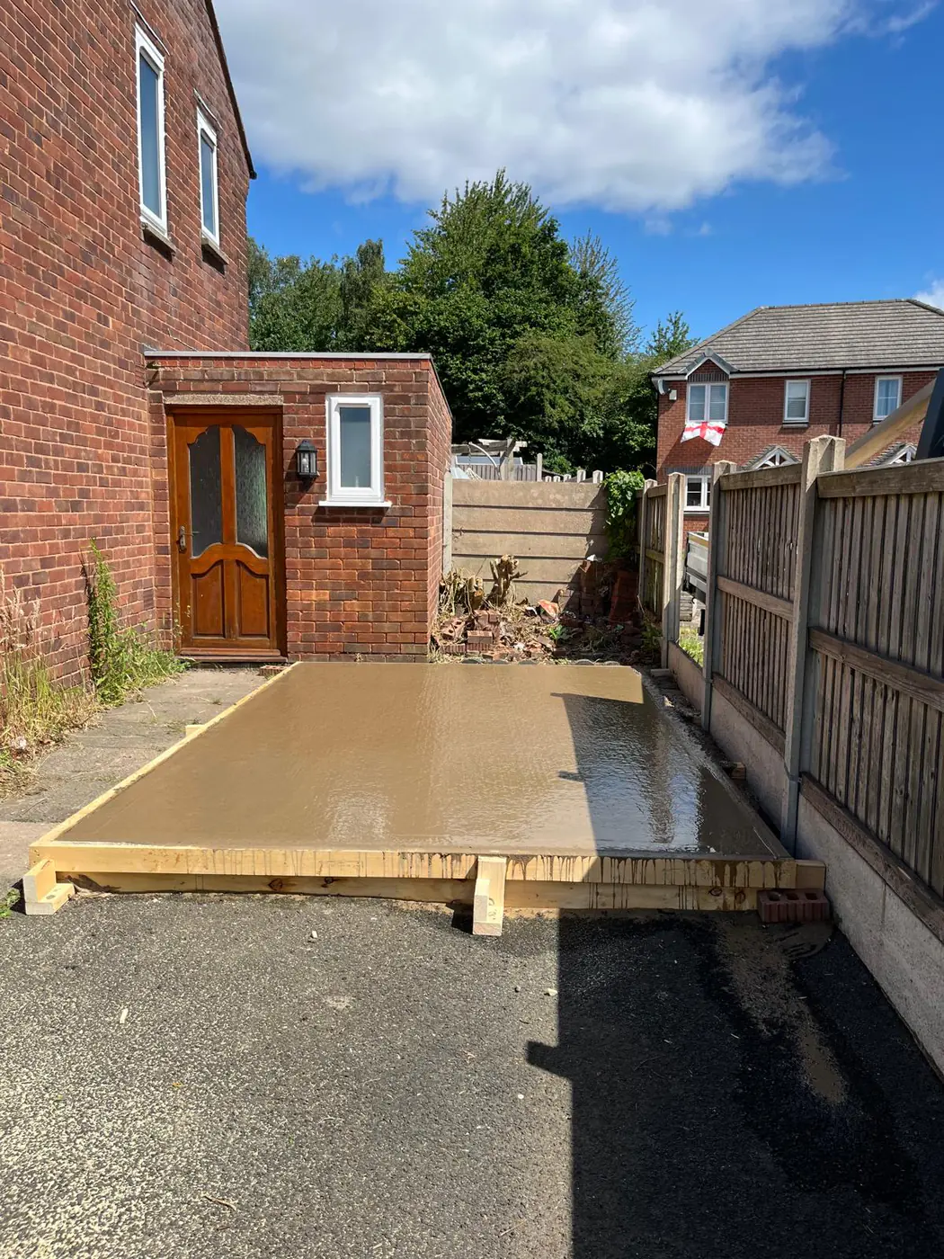 Freshly poured base beside a brick utility lean-to