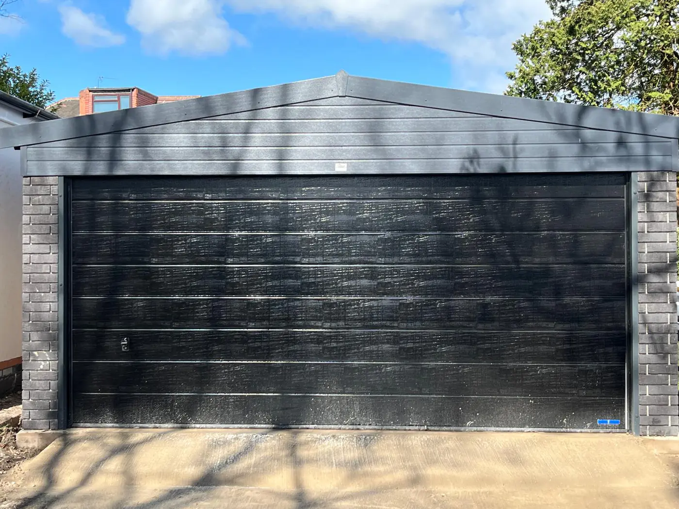 Completed garage with black sectional door and brick piers